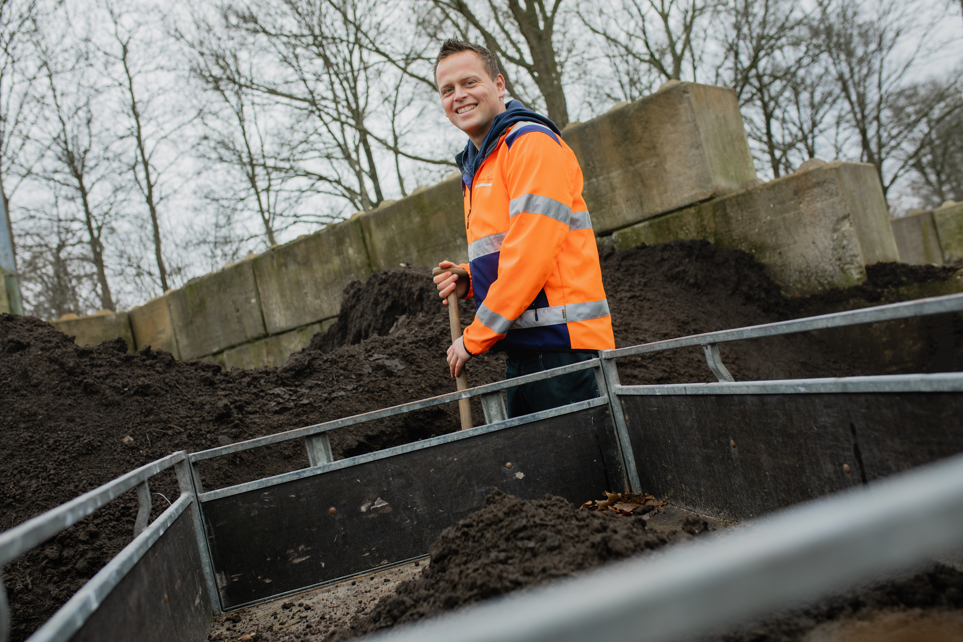Persoon in oranje hesje bij aanhanger met daarin compost
