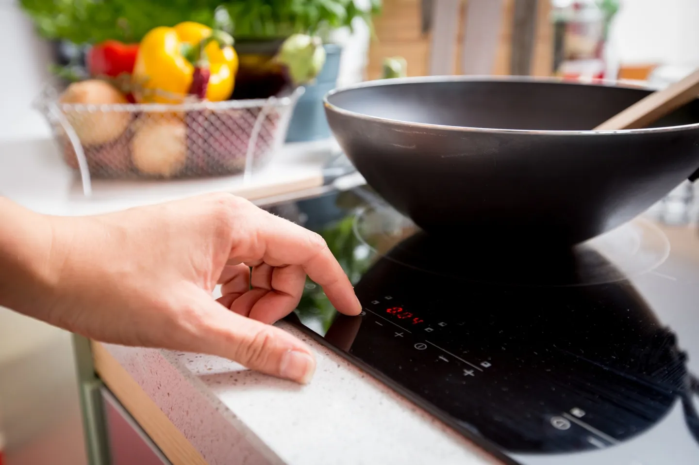 Elektrische kookplaat met daarop een wokpan, en daarbij een hand die de kookplaat instelt