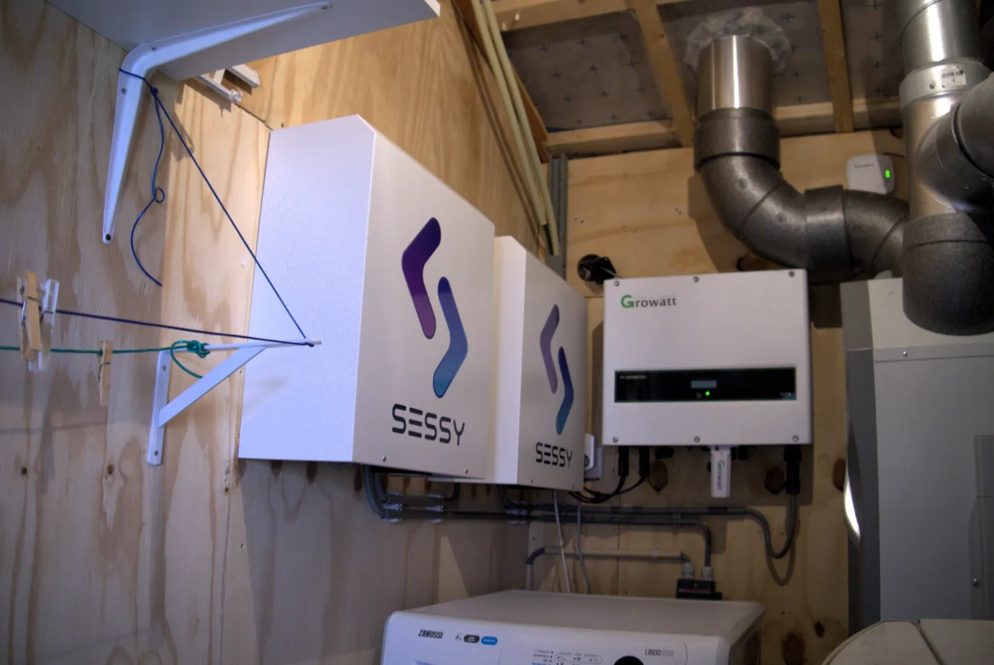 Thuisbatterij bestaande uit drie witte kastjes, gemonteerd aan een houten wand