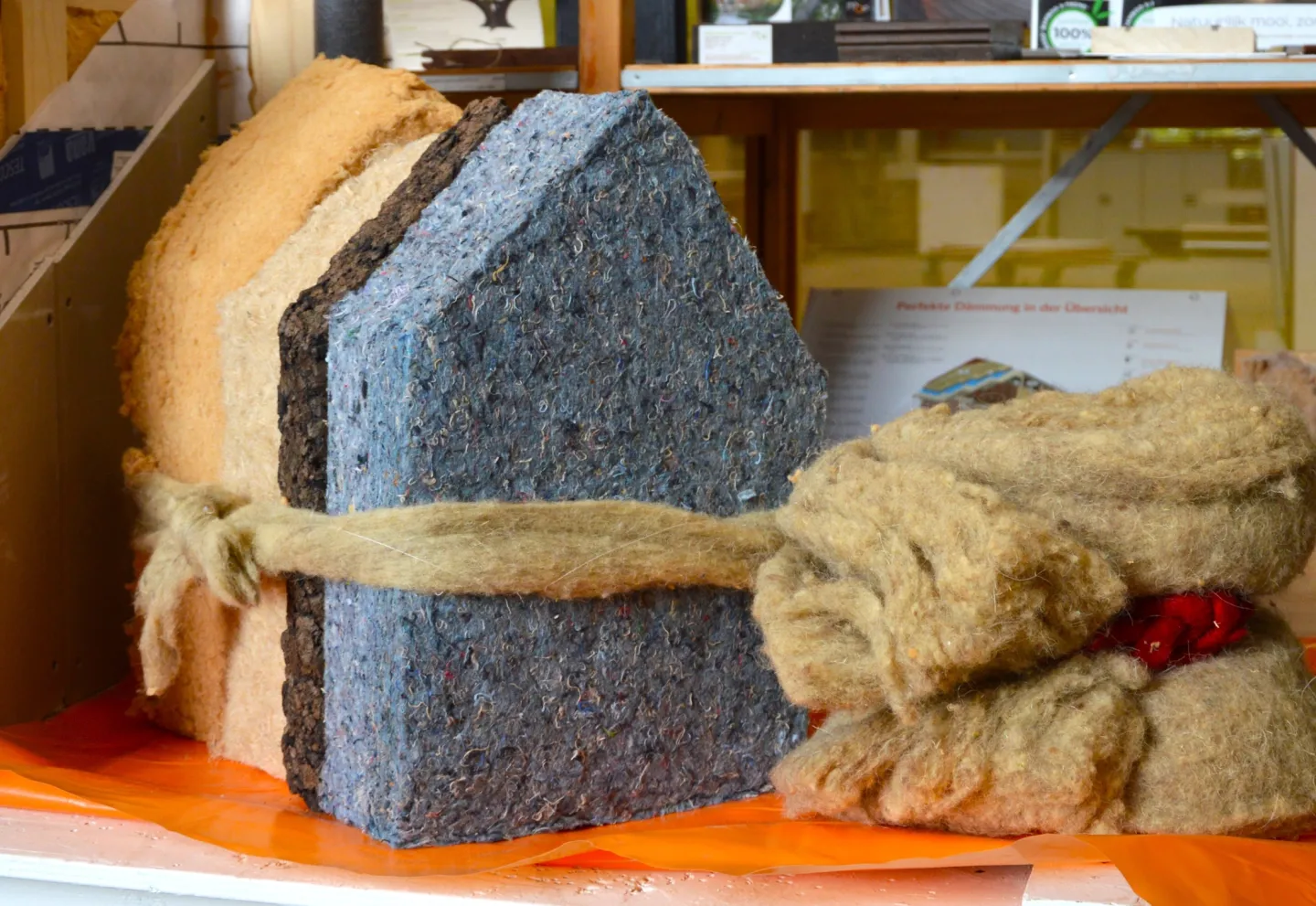 4 silhouetten van huisjes uitgesneden uit verschillende isolatiematerialen, bij elkaar gebonden met een lint van isolatiemateriaal