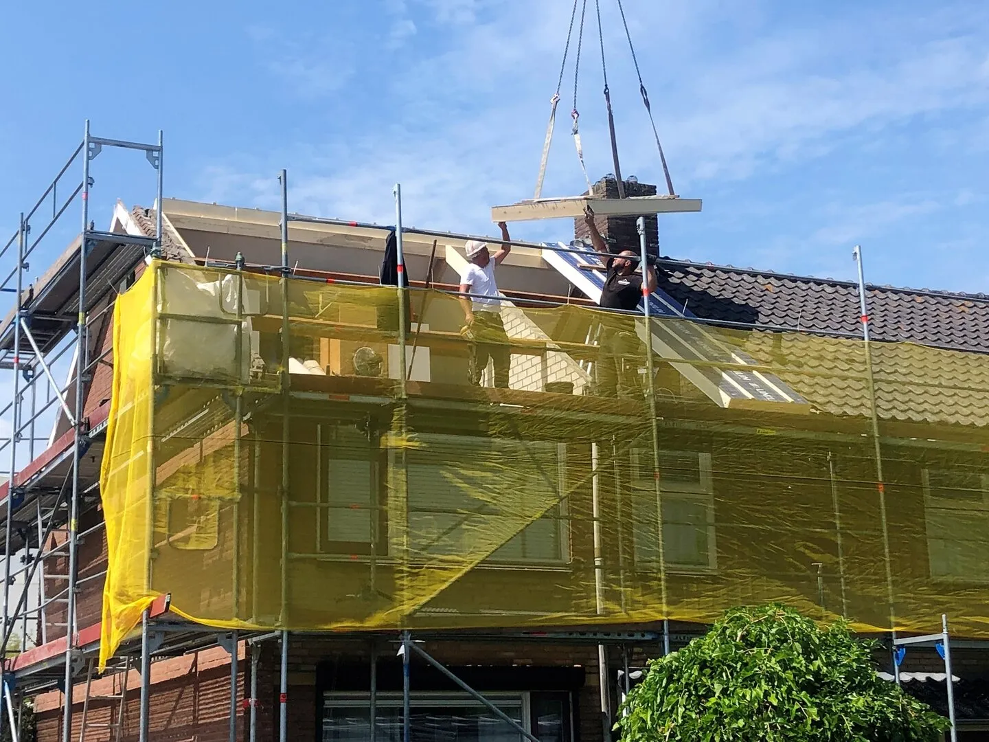 Hoekwoning met steigers eromheen, waarbij een nieuw dakraam naar een opening wordt getild door een kraan